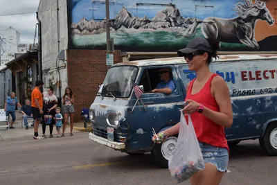 A vintage van with an American flag passes through downtown as community members line the streets for the Fourth of July parade in Brookings, South Dakota.